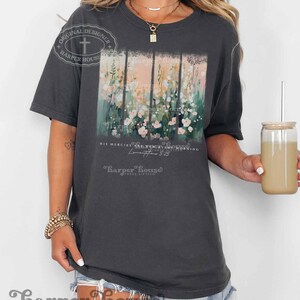 May include: A dark gray t-shirt with a floral design and the text "His mercies are new every morning" and "Lamentations 3:23" in white. The text "Harper House Three Sixteen" is also printed on the shirt in white.