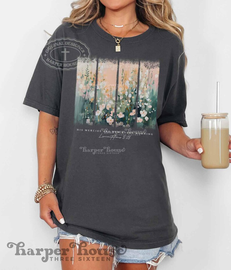 May include: A dark gray t-shirt with a floral design and the text "His mercies are new every morning" and "Lamentations 3:23" in white. The text "Harper House Three Sixteen" is also printed on the shirt in white.