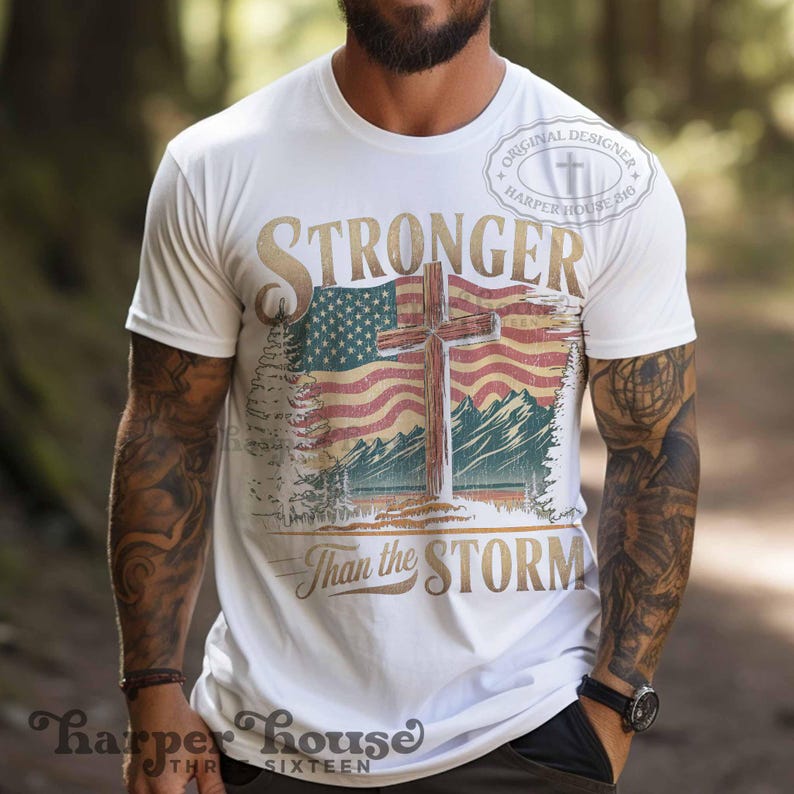 May include: White t-shirt with a distressed American flag design and a wooden cross. The text "Stronger Than the Storm" is printed below the flag. The shirt has a distressed look and a vintage feel.