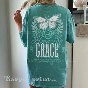 Pu&ograve; includere: Una maglietta blu turchese con una farfalla bianca, rose e il testo "Amazing Grace" con gli anni 19 e 99 su entrambi i lati. Il testo "How Sweet The Sound" &egrave; sotto il testo principale.
