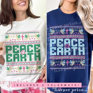 May include: Two Christmas-themed t-shirts with a white and a navy blue background. Both shirts feature a knitted pattern with the words "Peace on Earth" in pink and green letters. The pattern also includes angels, crosses, and stars.