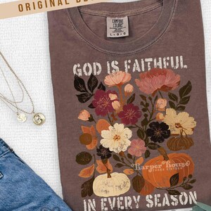 May include: A brown Comfort Colors t-shirt with the text "GOD IS FAITHFUL IN EVERY SEASON." The shirt features a floral and pumpkin design in shades of cream, orange, burgundy, and brown. The words "ORIGINAL DESIGNER!" are at the top.