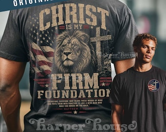 Può includere: Una t-shirt nera con una grande grafica sul retro raffigurante un leone, una croce e una bandiera americana con il testo "CHRIST IS MY FIRM FOUNDATION" e "MATTHEW 7:24". Il petto mostra un piccolo logo circolare con una croce e una bandiera.