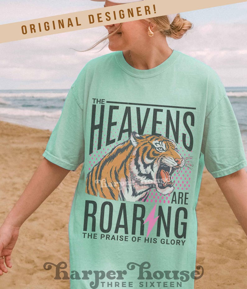 May include: A light green t-shirt with the text "THE HEAVENS ARE ROARING" and a tiger graphic. The shirt also includes the text "THE PRAISE OF HIS GLORY" and the brand name "harper house THREE SIXTEEN".