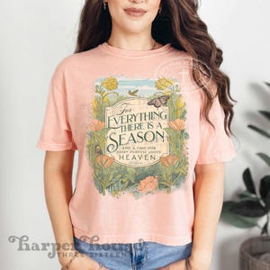 May include: A pink cropped t-shirt with a floral design and the text "For Everything There Is A Season And A Time For Every Purpose Under Heaven" in a green banner.