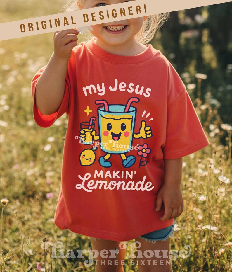 Op de afbeelding: Rood t-shirt met de witte tekst "my Jesus makin' lemonade". Het shirt heeft een cartoonafbeelding van een glimlachend limonadeglas met armen en benen, dat een duim omhoog geeft. Er is ook een klein citroenpersonage aanwezig.
