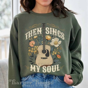 May include: A green sweatshirt with a floral design and a guitar with the text "Then Sings My Soul".