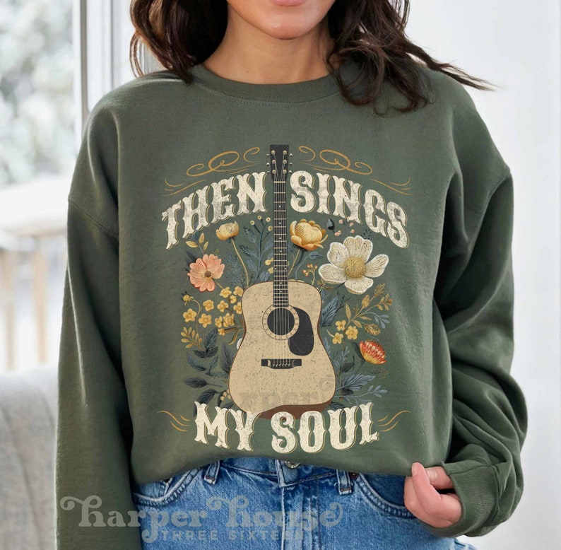May include: A green sweatshirt with a floral design and a guitar with the text "Then Sings My Soul".