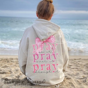 May include: A light beige hoodie with a pink bow and the text "pray on it pray over it pray through it" printed on the back.