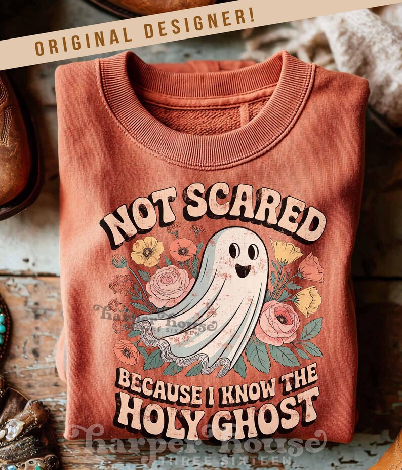 May include: A terracotta-colored sweatshirt with the text "NOT SCARED BECAUSE I KNOW THE HOLY GHOST" and a cartoon ghost illustration surrounded by flowers. The sweatshirt has a crew neck and long sleeves.