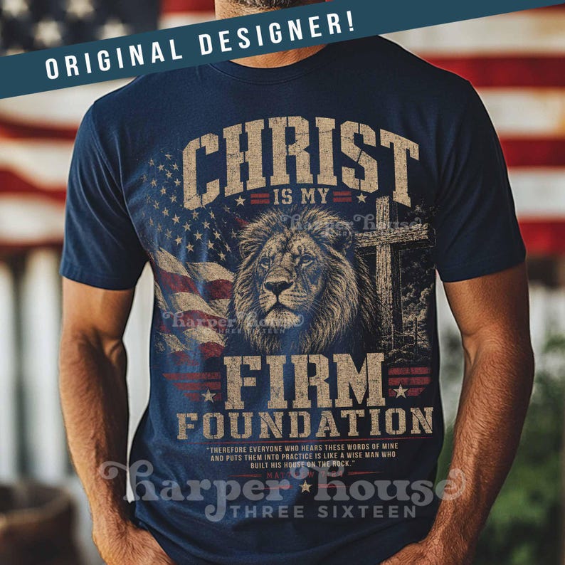May include: Navy blue t-shirt with a graphic featuring a lion, cross, and American flag. The text reads "CHRIST IS MY FIRM FOUNDATION" and includes the phrase "THREE SIXTEEN". The shirt has a distressed, vintage look.