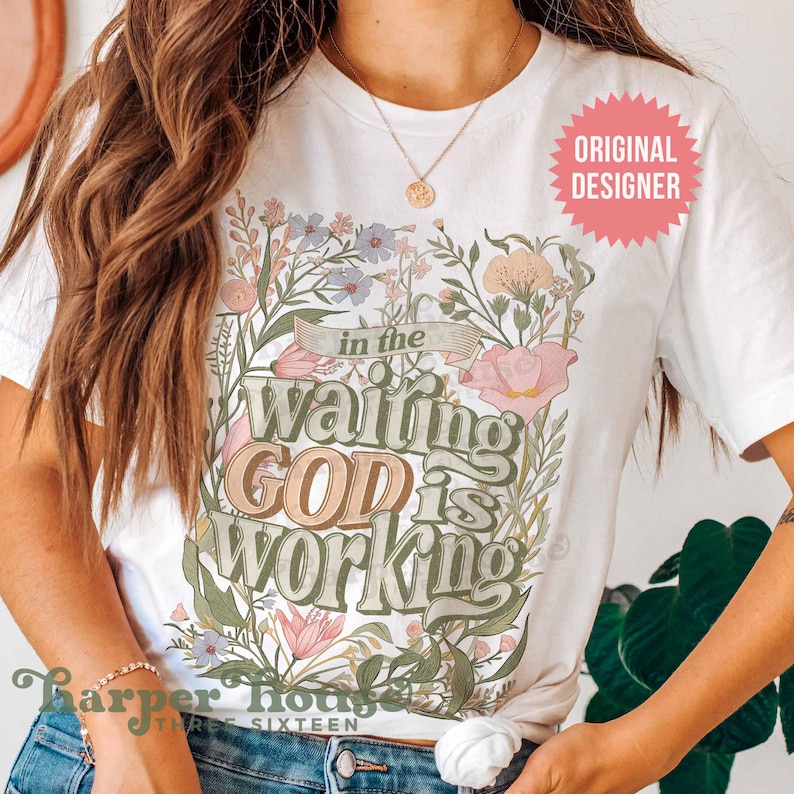 May include: White t-shirt with a floral design and the text "in the waiting GOD is WORKING".