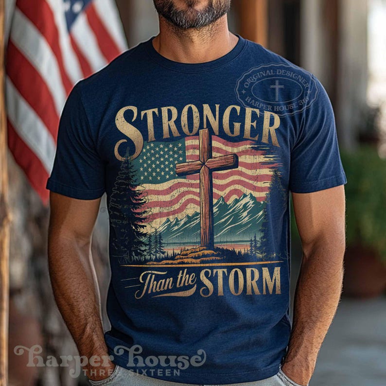 May include: A navy blue t-shirt with a distressed American flag and a wooden cross. The text "Stronger Than the Storm" is printed on the shirt.