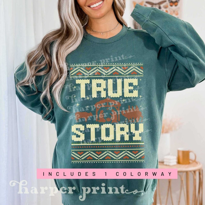 May include: A teal green sweatshirt with a Christmas-themed design. The design features a nativity scene with the text "TRUE STORY" in a brown and yellow font. The design is surrounded by a yellow and orange knit pattern.