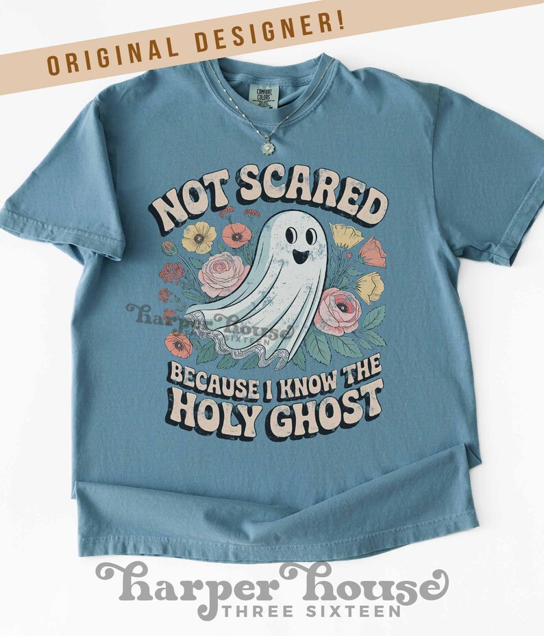 May include: A blue t-shirt with the text "NOT SCARED BECAUSE I KNOW THE HOLY GHOST" and a cartoon ghost surrounded by flowers. The shirt has short sleeves and a round neckline. The words "ORIGINAL DESIGNER!" are at the top.
