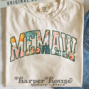 Op de afbeelding: Crèmekleurig T-shirt met het woord "MEMAW" in een patchwork-ontwerp met bloemen- en ruitpatronen. Het shirt heeft een ronde hals en korte mouwen. De tekst "ORIGINAL DESIGNER!" staat boven het shirt en de merknaam "Harper House THREE SIXTEEN" staat eronder.