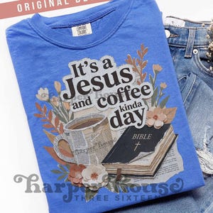 May include: A blue t-shirt with the text "It's a Jesus and coffee kinda day" and a graphic of a coffee cup, a Bible, and flowers. The shirt is folded on top of a pair of blue jeans.