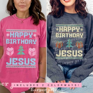 May include: Two t-shirts with a Christmas-themed design featuring the text "Happy Birthday Jesus". The design is in a pixelated style with a Christmas tree, presents, and snowflakes. The t-shirts are pink and gray.