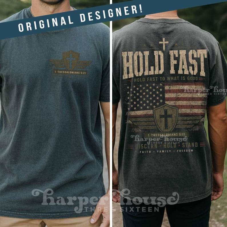 May include: Two-panel image of a dark gray t-shirt. The front features a shield and wing design with text. The back displays a cross, the words "HOLD FAST", an American flag, and additional text. The shirt is from Harper House.