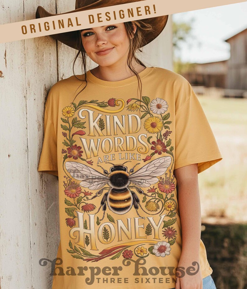 Peut inclure: T-shirt jaune moutarde avec un motif floral et une abeille. Le motif comprend les mots "Kind Words Are Like Honey". Le t-shirt est de Harper House Three Sixteen.