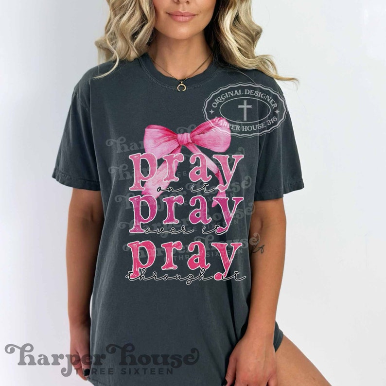 May include: A dark grey t-shirt with a pink ribbon and the text "Pray on it, Pray over it, Pray through it".