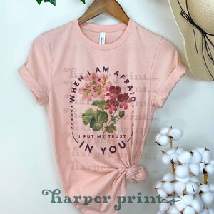 May include: A pink t-shirt with a floral design and the text "WHEN I AM AFRAID *PSALM 56:3* I PUT MY TRUST IN YOU".