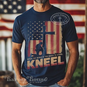 Pode incluir: Uma camiseta azul marinho com um gr&aacute;fico de um soldado ajoelhado em frente a uma cruz com um fundo de bandeira americana. O texto "WHEN THE WORLD IS TOO MUCH TO STAND, KNEEL" est&aacute; impresso na camiseta.