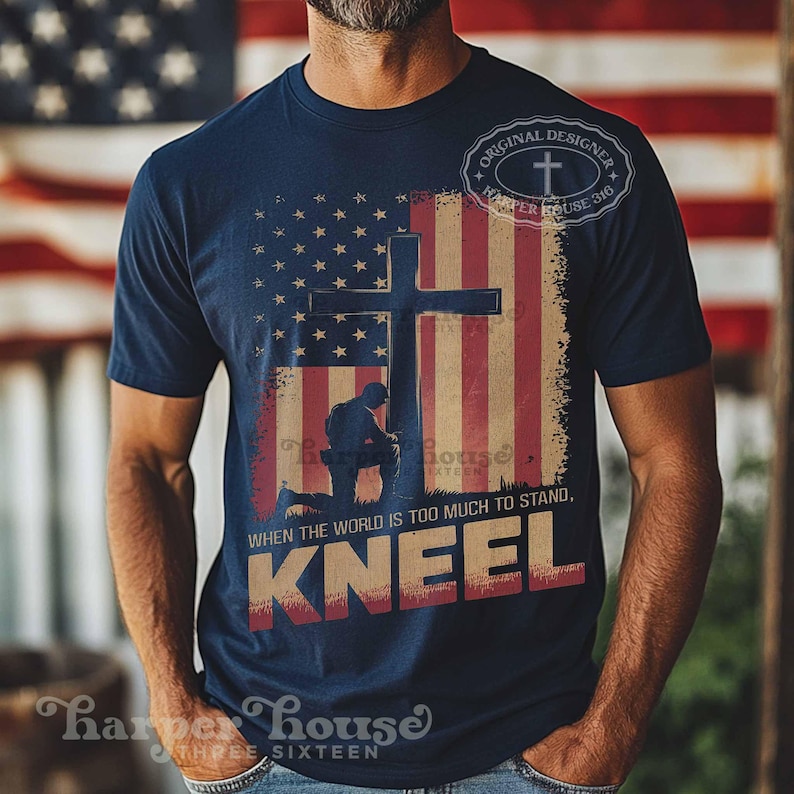 Pode incluir: Uma camiseta azul marinho com um gr&aacute;fico de um soldado ajoelhado em frente a uma cruz com um fundo de bandeira americana. O texto "WHEN THE WORLD IS TOO MUCH TO STAND, KNEEL" est&aacute; impresso na camiseta.