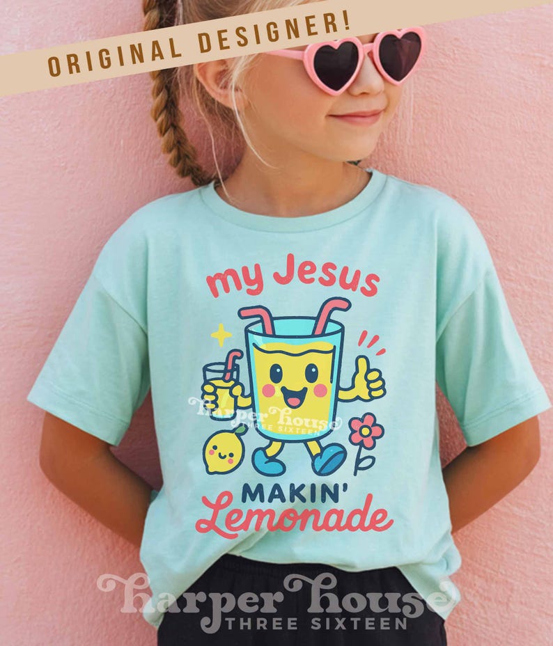 Op de afbeelding: Een lichtblauw t-shirt met de tekst "my Jesus MAKIN' Lemonade" en een cartoon limonade karakter. Het shirt heeft ook een kleine citroen, een bloem en de tekst "Harper House THREE SIXTEEN".
