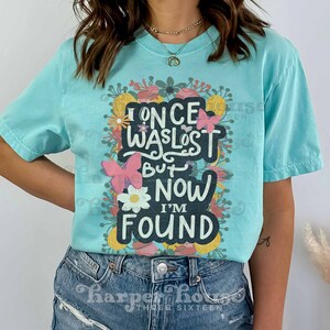 May include: A turquoise blue t-shirt with a floral design and the text "I once was lost but now I'm found".