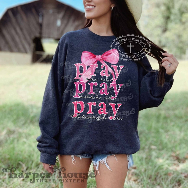 May include: A dark blue sweatshirt with a pink bow and the text "Pray on it Pray over it Pray through it".
