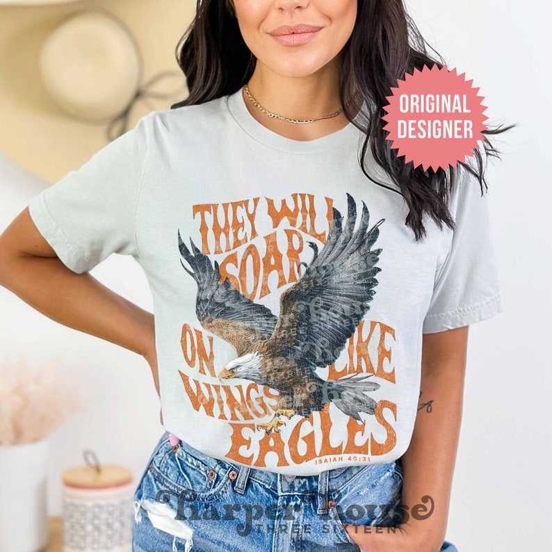 May include: A light blue t-shirt with a vintage-style graphic of an eagle soaring with the text "They will soar on wings like eagles Isaiah 40:31".