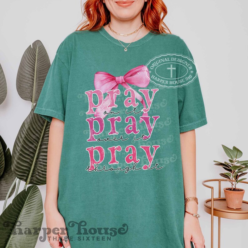 May include: A teal green t-shirt with a pink bow and the text "pray on it pray over it pray through it". The shirt also has a small white cross and the text "Original Designer Harper House 316" in a circle.