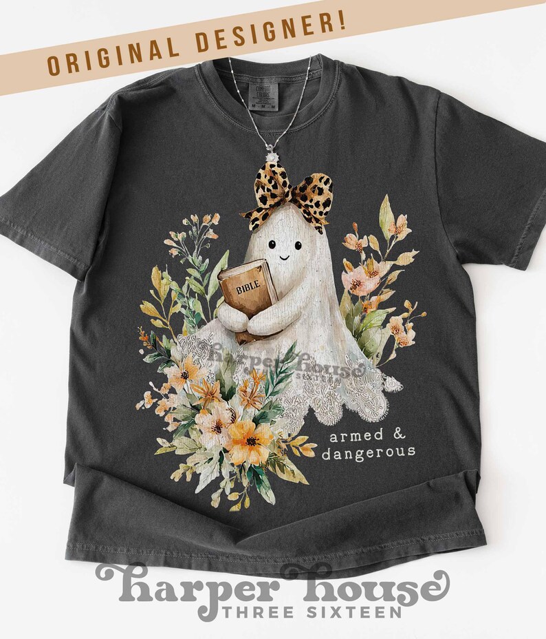 May include: Dark gray t-shirt featuring a cartoon ghost holding a Bible, adorned with a leopard print bow and surrounded by floral elements. The text "armed & dangerous" is printed on the shirt. The brand name "Harper House Three Sixteen" is at the bottom.