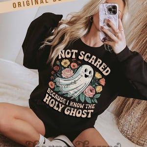 May include: Black sweatshirt with the text "NOT SCARED BECAUSE I KNOW THE HOLY GHOST" and a cartoon ghost illustration surrounded by flowers. The words "ORIGINAL DESIGNER!" are at the top. The brand name "Harper House Three Sixteen" is at the bottom.