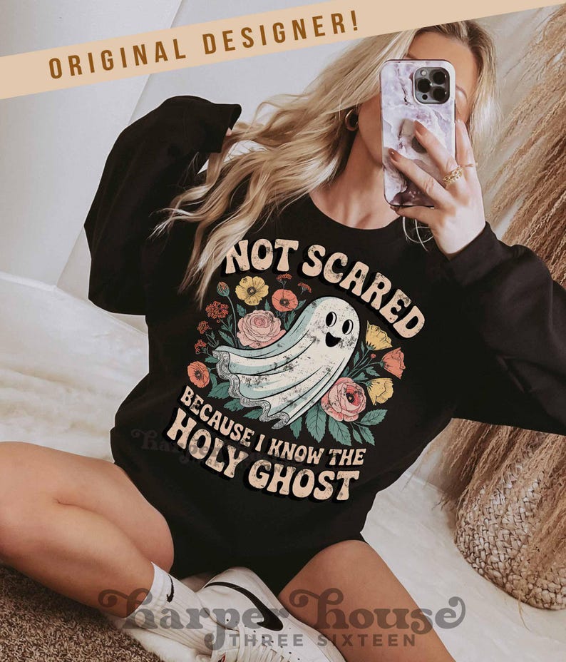 May include: Black sweatshirt with the text "NOT SCARED BECAUSE I KNOW THE HOLY GHOST" and a cartoon ghost illustration surrounded by flowers. The words "ORIGINAL DESIGNER!" are at the top. The brand name "Harper House Three Sixteen" is at the bottom.