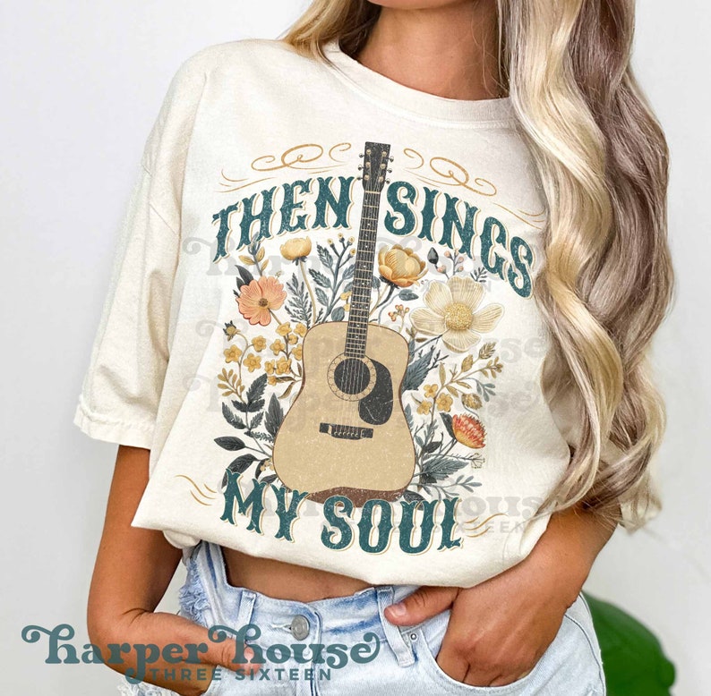 May include: A white t-shirt with a floral design and an acoustic guitar. The text "Then Sings My Soul" is printed on the shirt.