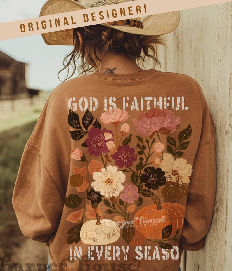 May include: A brown sweatshirt with floral and pumpkin graphics. The back of the sweatshirt features the text "GOD IS FAITHFUL IN EVERY SEASON". The design includes pink, white, and burgundy flowers, and orange and white pumpkins.