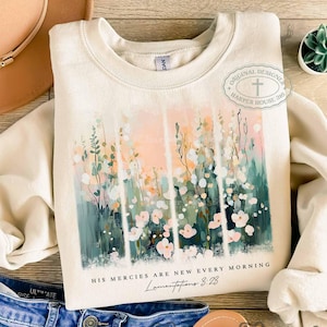 May include: A cream colored sweatshirt with a floral design and the text "His mercies are new every morning Lamentations 3:23".