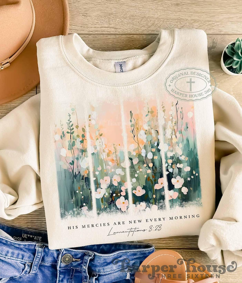 May include: A cream colored sweatshirt with a floral design and the text "His mercies are new every morning Lamentations 3:23".