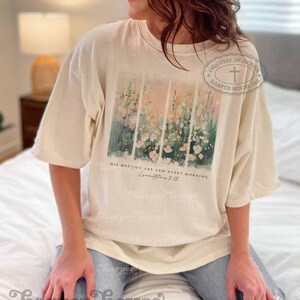 May include: A cream colored t-shirt with a floral design and the text "His mercies are new every morning" and "Lamentations 3:23".