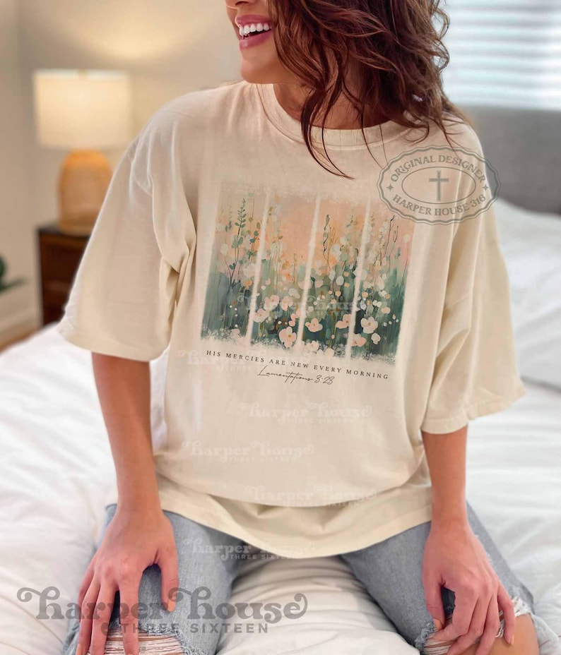 May include: A cream colored t-shirt with a floral design and the text "His mercies are new every morning" and "Lamentations 3:23".