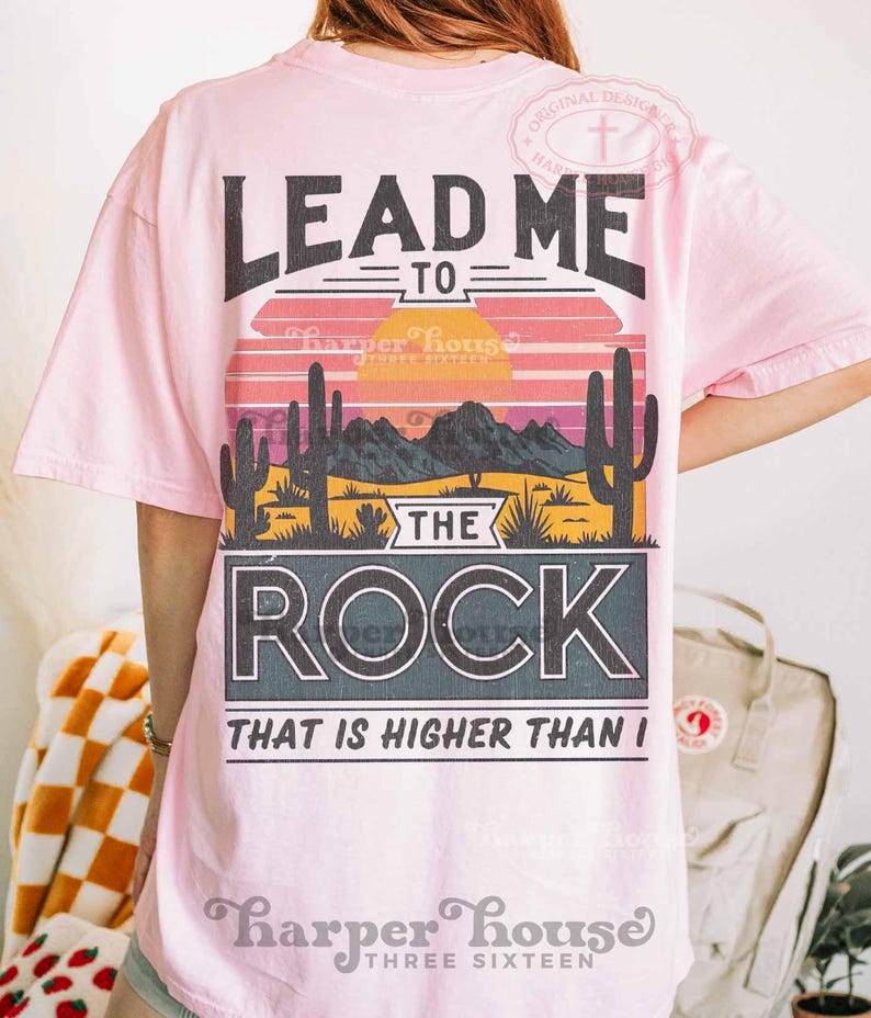 May include: Pink t-shirt with a graphic design that says "Lead Me To The Rock That Is Higher Than I". The graphic features a sunset scene with cacti and mountains.