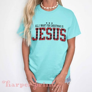 May include: A turquoise blue t-shirt with the text "All I want for Christmas is Jesus" in black with a red and black plaid pattern.