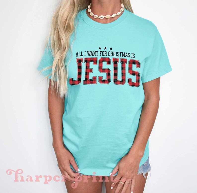 May include: A turquoise blue t-shirt with the text "All I want for Christmas is Jesus" in black with a red and black plaid pattern.