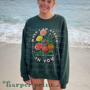 May include: A dark green sweatshirt with a floral design and the text "WHEN I AM AFRAID *PSALM 56:3 I PUT MY TRUST IN YOU" in a circle.