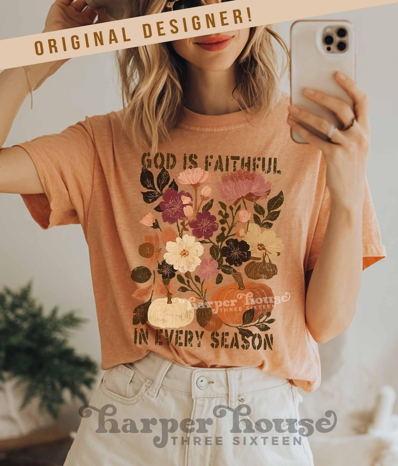 May include: Peach-colored t-shirt with a floral and pumpkin graphic. The text on the shirt reads "GOD IS FAITHFUL IN EVERY SEASON." The design includes various flowers and pumpkins. The words "ORIGINAL DESIGNER!" are at the top.