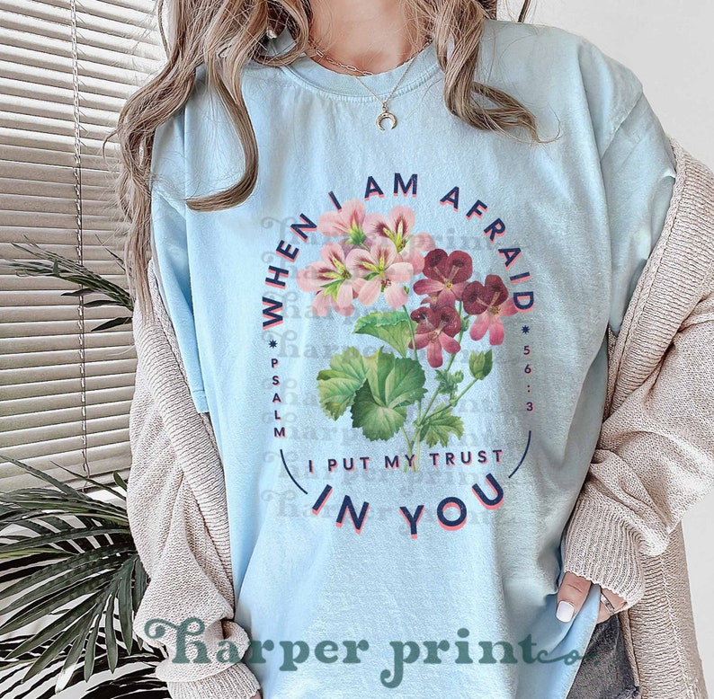 May include: Light blue t-shirt with a floral design and the text "WHEN I AM AFRAID *PSALM 56:3 I PUT MY TRUST IN YOU".