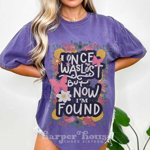 May include: Purple t-shirt with a floral design and the text "I once was lost but now I'm found".