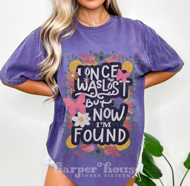 May include: Purple t-shirt with a floral design and the text "I once was lost but now I'm found".